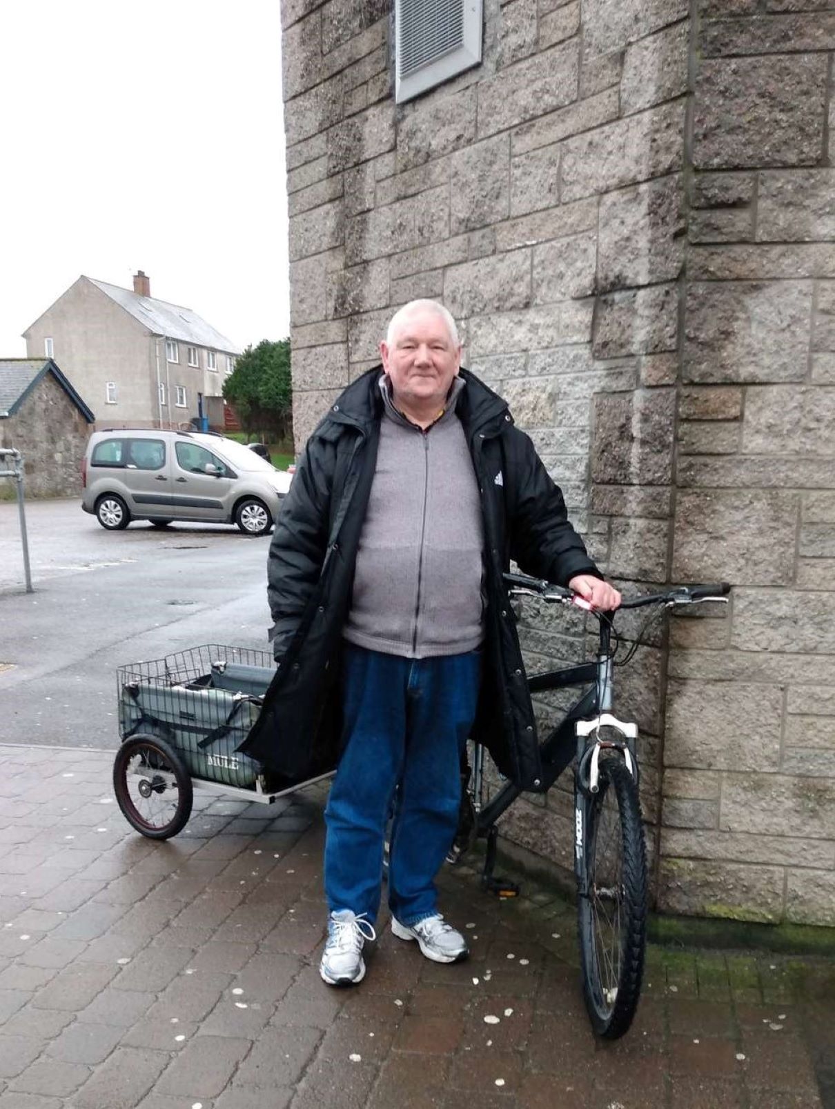 A man stands next to his bicycle which has a small trolley on the back