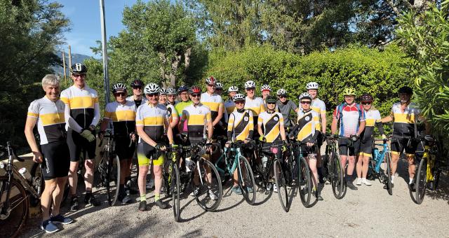 A big group of people are standing with their bikes. They’re all wearing cycling kit, with most in club kit