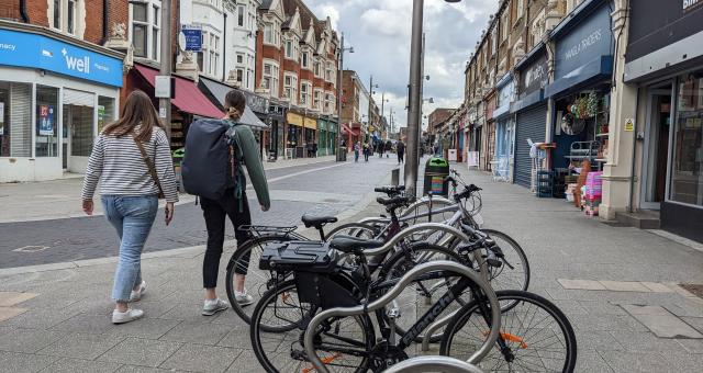 A busy high street with people walking and cycling and carrying shopping bags. The street is only open to cycling and walking