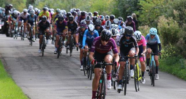 Demi Vollering cycling at a professional race. She is in currently leading with the rest of the peloton behind her.