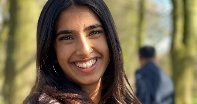 Hanna Ahmed is wearing a checked jacket and smiling as she is standing on a footpath surrounded by trees