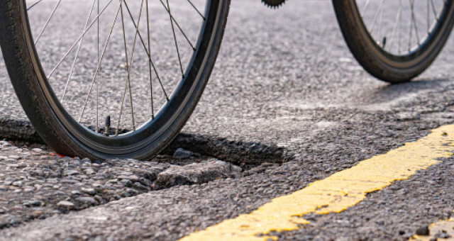 A bike wheel moving through a pothole in a road. 