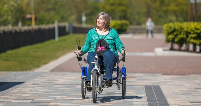 A women cycling a recumbent trike out in the sun on a pedestrianised path