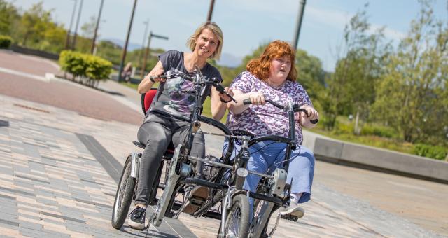 Two people cycling outside on a path on a two seater trike