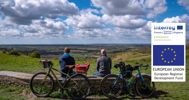 Two men sit on a bench looking out at a view of rolling hills