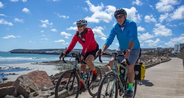 A man and woman cycle along a coastal path