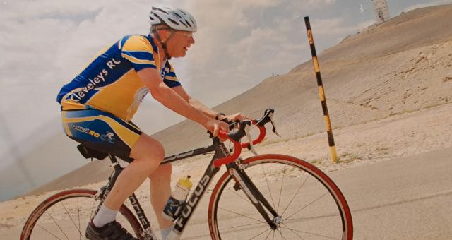 A man wearing a helmet rides a bicycle up a steep hill in a barren landscape